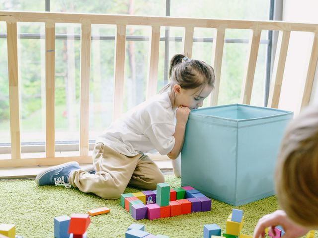 A child playing with wooden building blocks on an indoor play rug