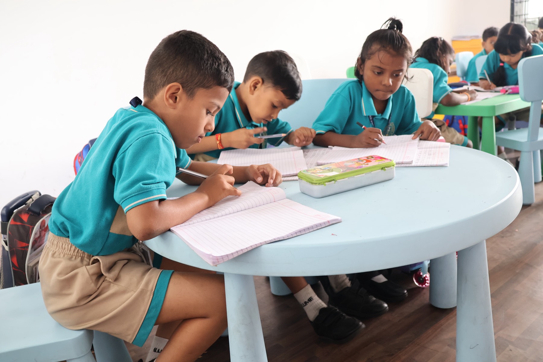 Young V3 students in school uniform writing in their notebooks at a round classroom table